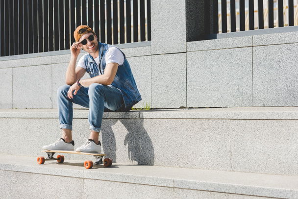 jeune patineur souriant assis sur les escaliers avec longboard regardant loin
 - Photo, image
