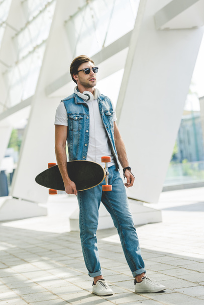 young skateboarder in denim clothes with longboard and headphones - Фото, зображення