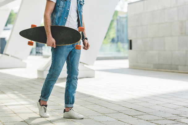 cropped shot of skater in denim clothes with skateboard - Foto, imagen