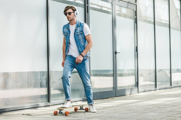 handsome young skater in denim clothes riding skateboard - Foto, afbeelding