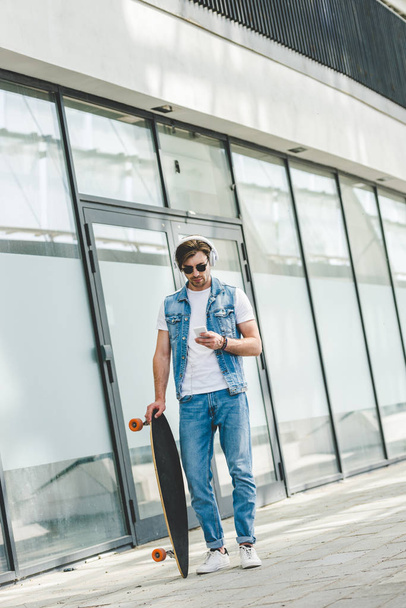 handsome young skateboarder with longboard using smartphone - Foto, imagen