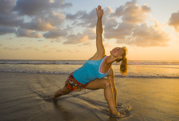 young fit and attractive sport woman in beach sunset yoga practice workout on wet sun in front of the sea in meditation and relaxation exercise - Foto, Imagen