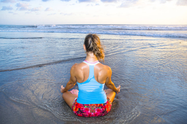 young fit and attractive sport woman in beach sunset yoga practice workout sitting on wet sun in front of the sea in meditation and relaxation exercise - 写真・画像