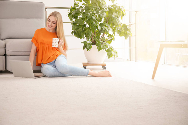 Young woman with laptop sitting on floor at home - Foto, Bild