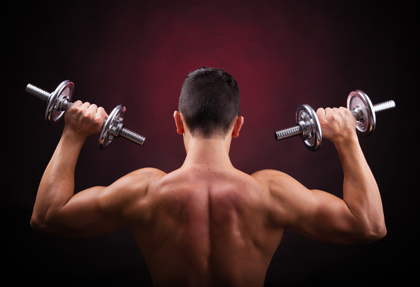 Muscular young man lifting weights against black background - Foto, Imagem