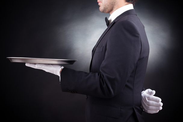 Cropped image of a young waiter holding an empty dish on black b - Photo, Image