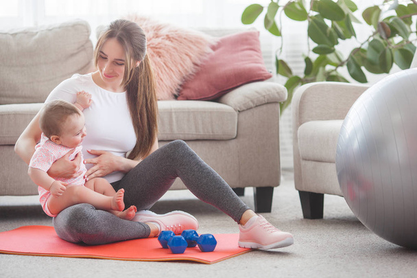 Young pretty mother working out with her little child at home - Foto, imagen