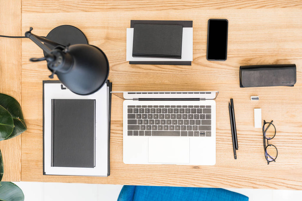 top view of arranged eyeglasses, laptop, notebooks and smartphone at workplace - Fotó, kép