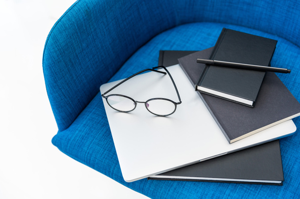 vue rapprochée de l'ordinateur portable, des cahiers noirs et des lunettes sur chaise bleue isolée sur blanc
 - Photo, image