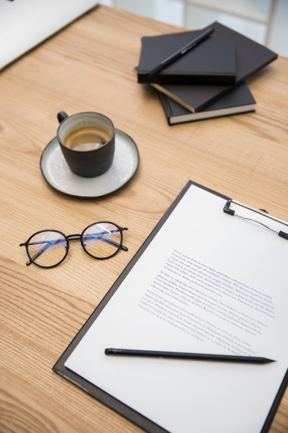 close up view of cup of coffee, eyeglasses, documents on wooden tabletop - Photo, Image