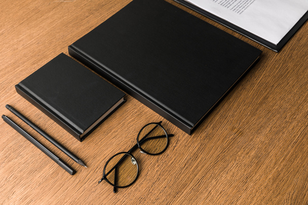 vista cercana de cuadernos negros, anteojos y artículos de papelería en la mesa de madera
 - Foto, Imagen