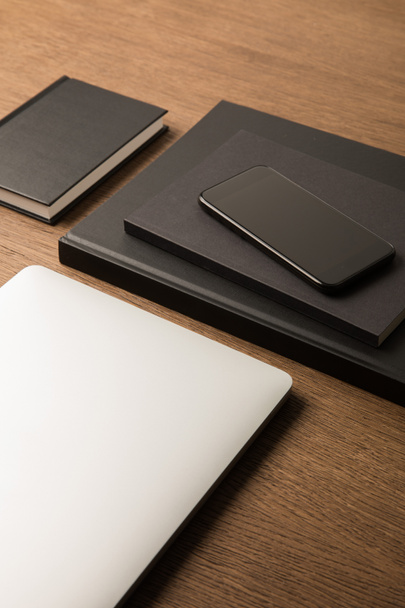 close up view of laptop, pile of black notebooks and smartphone on wooden tabletop - 写真・画像