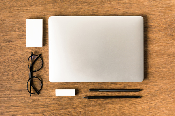 flat lay with arranged laptop, eyeglasses, blank cards, pen and pencil on wooden tabletop - Foto, afbeelding