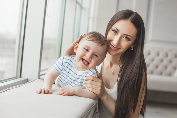 Young pretty mother playing with her little son. Cheerful family smiling at camera - Фото, зображення