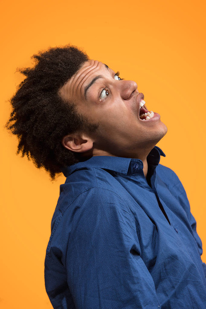 Η συναισθηματική θυμωμένος νεαρός ουρλιάζοντας σε φόντο πορτοκαλί στούντιο - Φωτογραφία, εικόνα