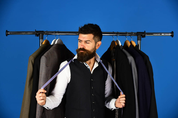 Businessman with serious face near jackets on blue background - Foto, Bild