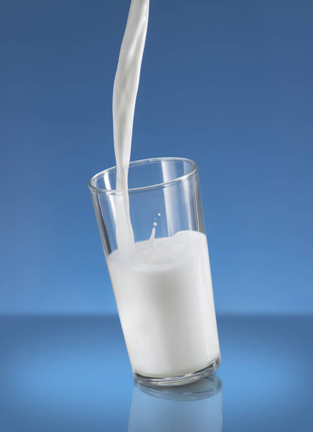 Nalil mléko stříkající ve skle nad modrým pozadím - Fotografie, Obrázek