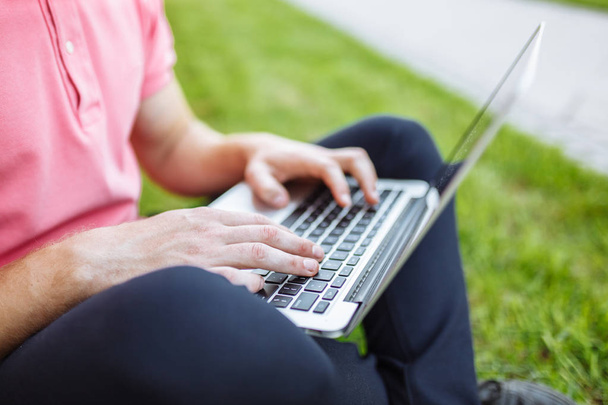 Handsome man sitting on the grass in the city with a laptop, job search - Fotografie, Obrázek