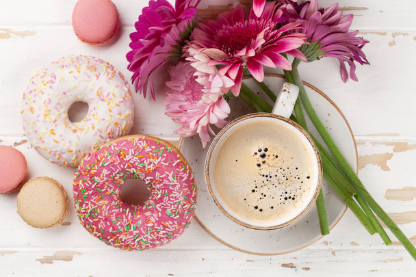 Coffee cup, donuts and gerbera flowers on white wooden table. Top view - Foto, immagini