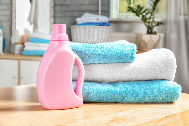 Stack of clean towels and bottle with detergent on table - Fotó, kép