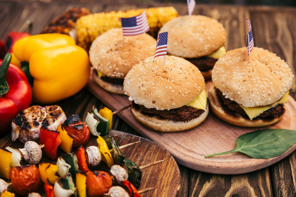Hamburger mit Flaggen und Gemüse, das draußen auf dem Grill gegrillt wird - Foto, Bild