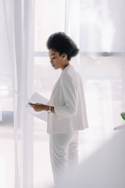 side view of attractive african american businesswoman reading documents in office - Foto, afbeelding