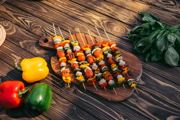 Wooden board with vegetables and mushrooms on skewers cooked outdoors on grill - Photo, Image