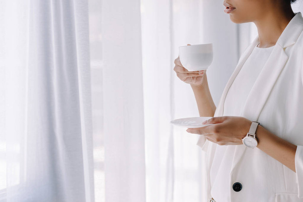 geschnittenes Bild einer afrikanisch-amerikanischen Geschäftsfrau, die eine Tasse Kaffee im Büro hält - Foto, Bild