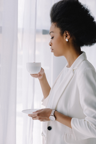 atraktivní africká americká podnikatelka držící šálek kávy v kanceláři - Fotografie, Obrázek
