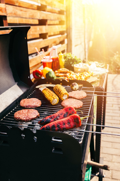 Burger patties and vegetables cooked outdoors on grill - Foto, afbeelding