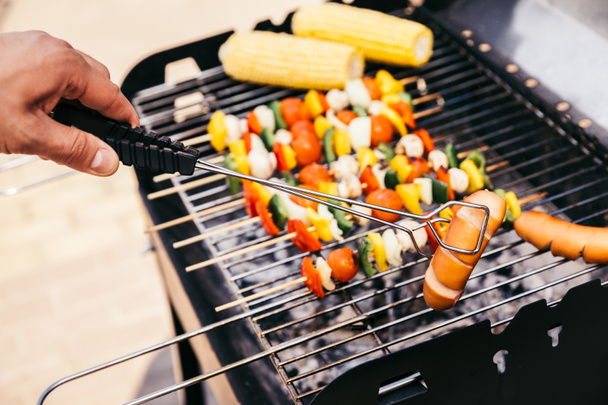 Chef checking vegetables and sausages cooked outdoors on grill - Foto, Bild