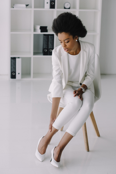 attractive african american businesswoman touching ankle in office - Photo, Image