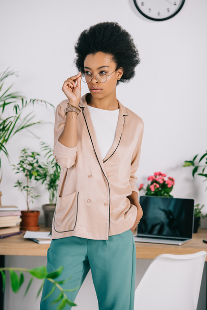 attractive african american businesswoman standing near table in office and touching glasses - 写真・画像