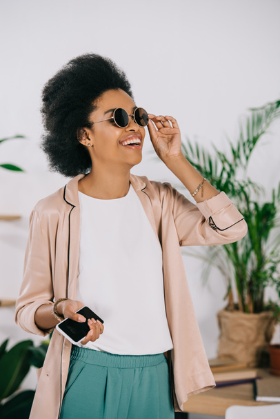 rindo atraente afro-americana empresária tocando óculos de sol no escritório
 - Foto, Imagem