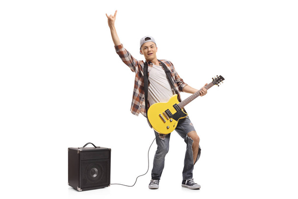 Retrato de larga duración de un adolescente con una guitarra eléctrica y un amplificador haciendo un gesto de rock aislado sobre fondo blanco
 - Foto, imagen