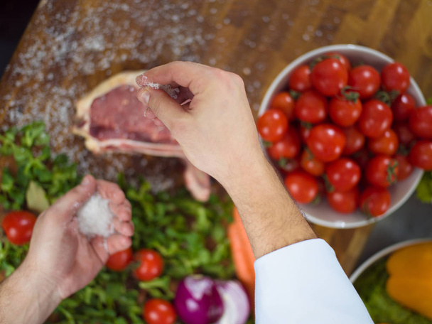 Chef putting salt on juicy slice of raw steak - Фото, изображение