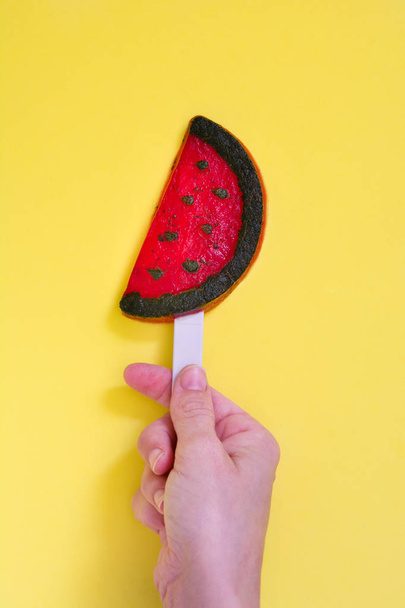Hand holding watermelon popsicle on yellow background. Top view - Photo, image