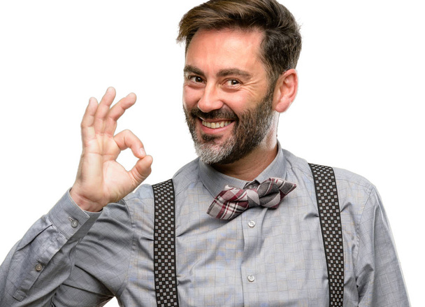 Middelbare leeftijd man, met baard en strikje doen ok teken met hand, goedkeuren gebaar geïsoleerd op witte achtergrond - Foto, afbeelding