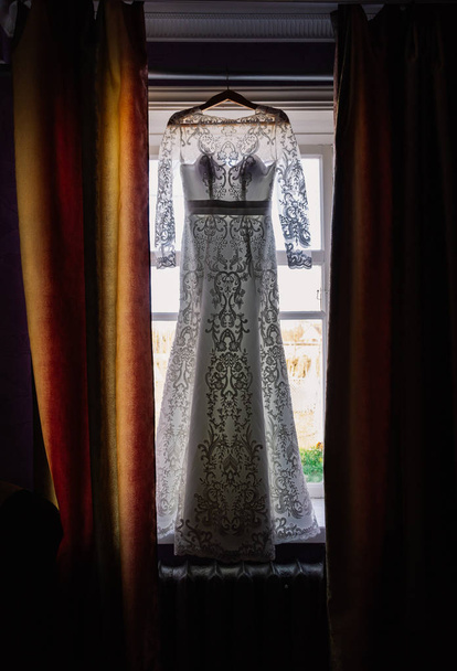 Vestido de novia colgado en la ventana de la habitación
 - Foto, imagen