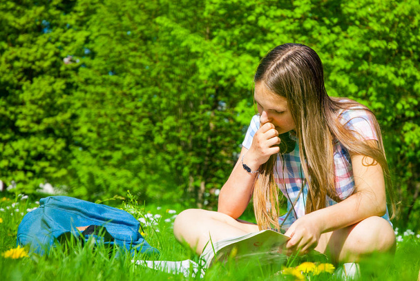 Student studying in park. Joyful happy teenager girl student sitting and reading outside on university campus or park. - Photo, image