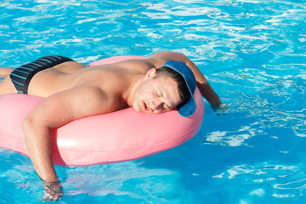 pohled shora opilý mladík plavat s růžový kruh v bazénu. opilý člověk na dovolené v hotelu - Fotografie, Obrázek