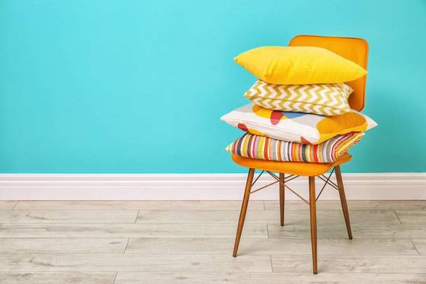 Различные подушки на стуле рядом с цветной стеной в номере
 - Фото, изображение