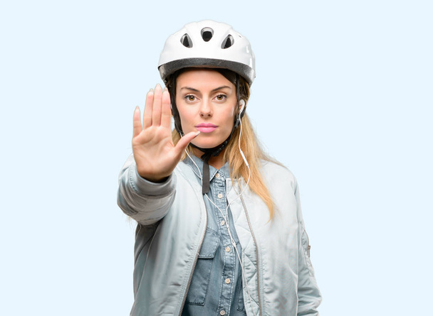 Jonge vrouw met fiets helm en oortelefoons geërgerd met slechte houding maken stopbord met hand, zegt Nee, uiting van veiligheid, defensie of beperking, misschien duwen - Foto, afbeelding