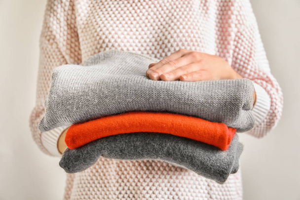 Young woman holding stack of warm knitted clothes, closeup - Photo, Image