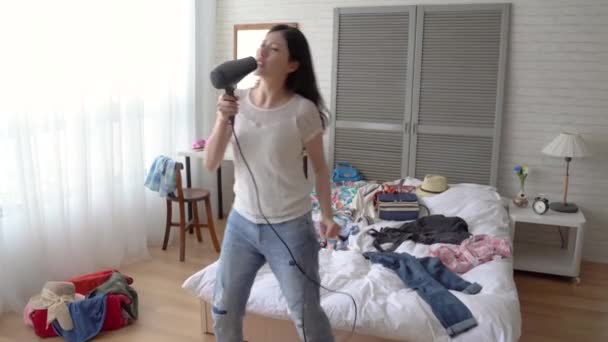 Slow motion of the young modern Asian woman singing in her bedroom using the hairdryer. She sinks herself into the pop music. She is imitating the superstars. - Video