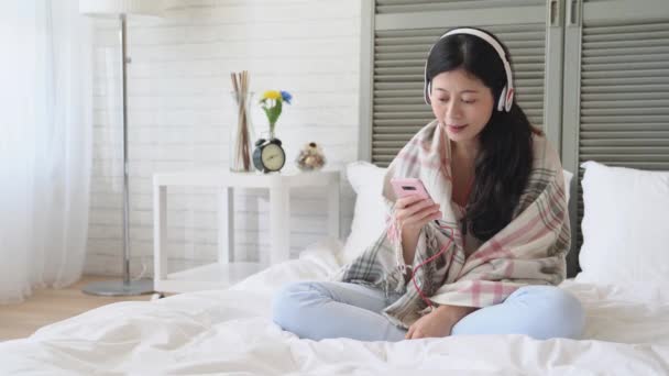 Young Asian lady woke up and listen to the music with her headphone. She is in a good mood in this pleasant weekend morning. - 映像、動画