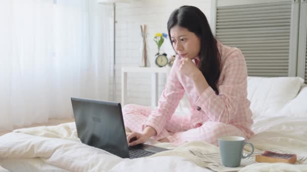 Young Asian girl typing words by using a laptop in the bed. on a side view. She is hard working and deligent. Keep focus and concentrate on her work. - Materiał filmowy, wideo