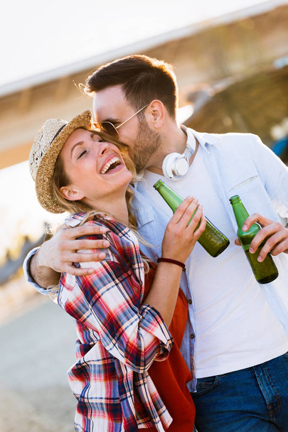 Happy young couple smiling and drinking beer at beach - Photo, Image