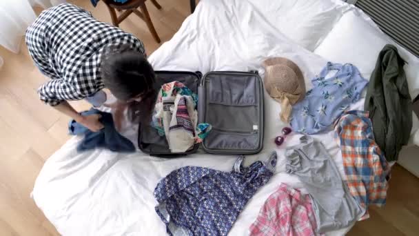 Asian woman packing up her luggage.  She threw everything on the bed into the suitcase. On a high angle. - Filmati, video