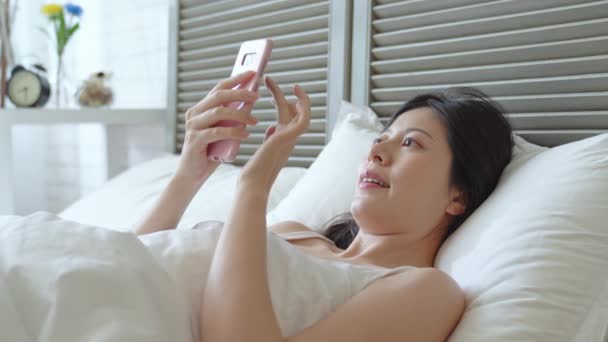 The young lady playing using a smartphone in the bed. She is checking the emails and this is her daily routine. - Кадры, видео